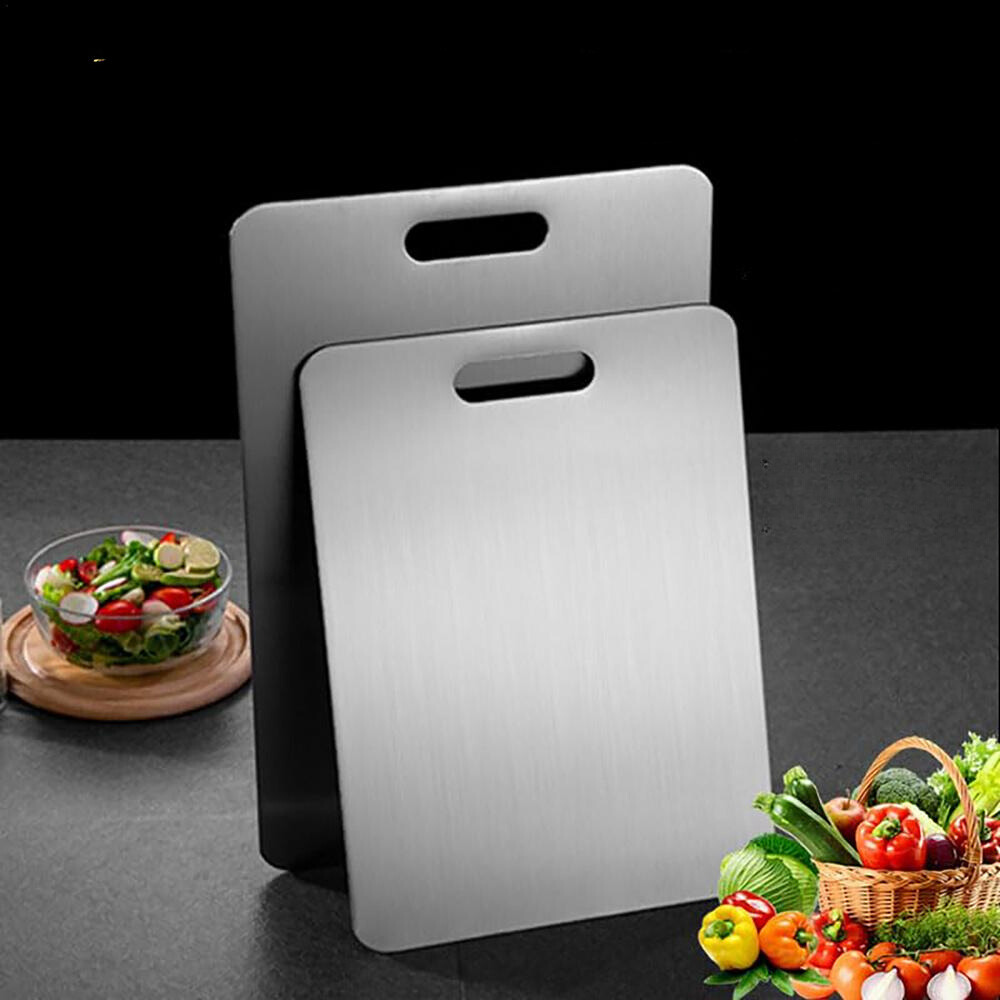 Two stainless steel cutting boards with a bowl of salad and basket of vegetables on a dark surface.